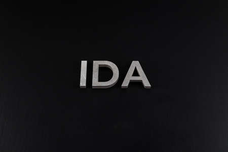 the word ida laid with silver metal letters over dry black matte surfaceの写真素材