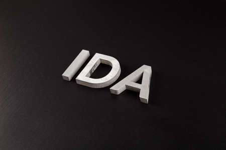 the word ida laid with silver metal letters over dry black matte surfaceの写真素材