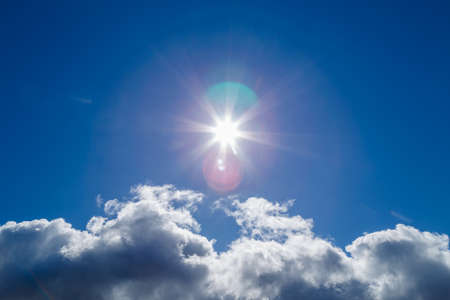 sun over white cloud on blue sky background with natural lens flaresの写真素材