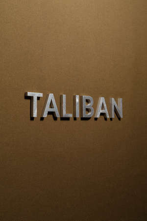the word taliban laid with silver metal letters on rough tan khaki canvas fabricの写真素材