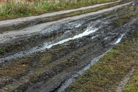 A broken rural country road after the rain. Puddles on a dirt road. Clay, soil and puddles at cloudy...
