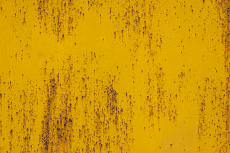 full frame background and texture of yellow painted sheet steel with multiple rust spots on it
