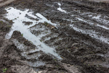 A broken rural country road after the rain. Puddles after rain on a dirt road. Clay, soil and puddles at cloudy day light after rain, autumn season.の写真素材