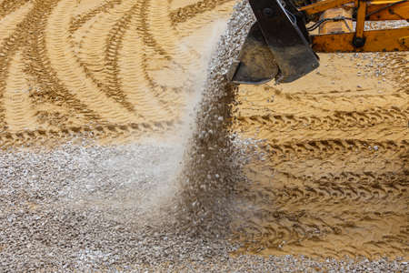 a bulldozer pours gravel from a bucket onto the compacted sand at a construction siteの写真素材
