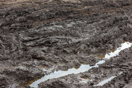 A broken rural country road after the rain. Puddles after rain on a dirt road. Clay, soil and puddles at cloudy day light after rain, autumn season.の写真素材