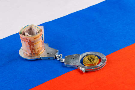 roll of russian paper rubles currency and bitcoin shiner chained with handcuffs on russian flag backgroundの写真素材