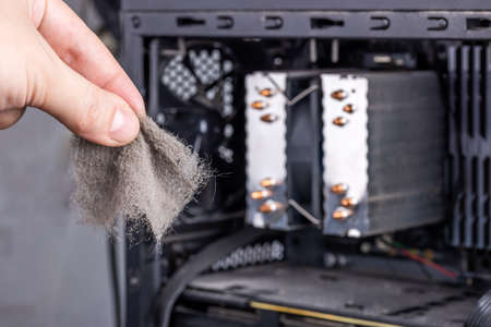 bare caucasian hand holding dust clog in front of opened pc case during maintenanceの写真素材