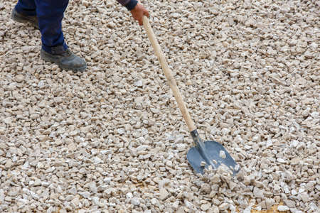 construction wroker shoveling white macadam during road construction process