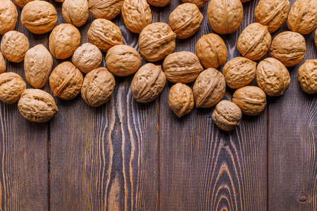 many walnuts with shells randomly scattered on brown wooden table surface, close-up with copy space at bottom of pictureの写真素材