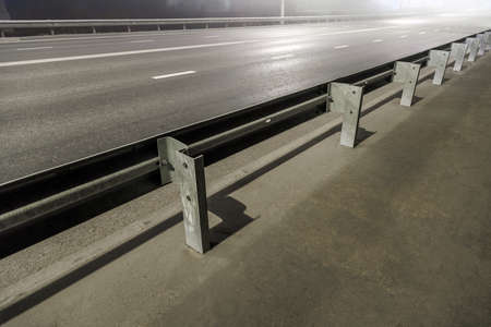 illuminated empty foggy night road with rigid guardrails