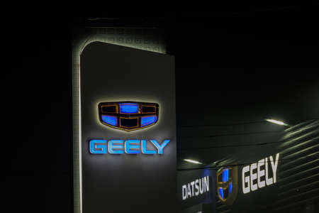Geely logo on car dealership pillar and building at foggy night - Geely is one of the largest...