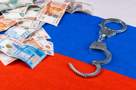 silver colored handcuffs and russian paper rubles currency on russian flag backgroundの写真素材