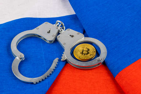 roll of russian paper rubles currency and bitcoin shiner chained with handcuffs on russian flag backgroundの写真素材