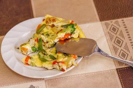 plate with slices of omelet of scrambled eggs with vegetables and stainless steel spatulaの写真素材