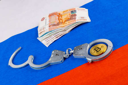 bunch of russian paper rubles currency and bitcoin shiner chained with handcuffs on russian flag backgroundの写真素材