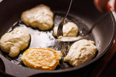 hands with two forks flipping semi-liquid dough roasting on cast iron pan covered with vegetable oilの写真素材