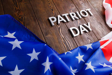 the words patriot day laid with silver metal letters on wooden board surface with crumpled usa flagの写真素材