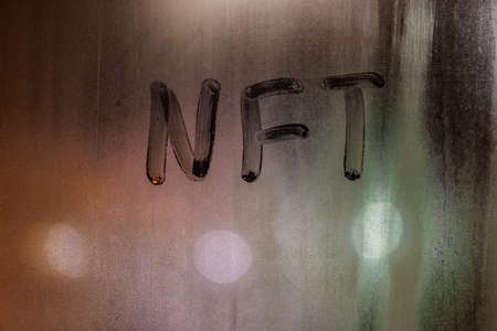 the word NFT - non-fungible token handwritten on foggy window glass at nightの写真素材