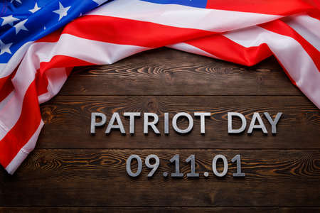 the words patriot day laid with silver metal letters on wooden board surface with crumpled usa flagの写真素材
