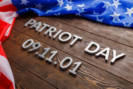 the words patriot day laid with silver metal letters on wooden board surface with crumpled usa flag