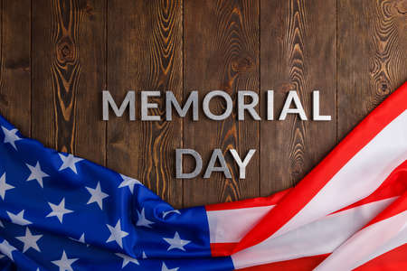 the words memorial day laid with silver metal letters on wooden board surface with crumpled usa flag
