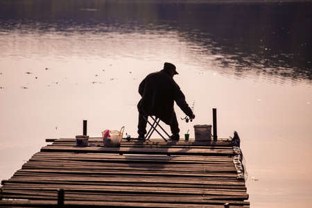 silhouette of a fisherman from behind sitting on a wooden pier during evening fishing