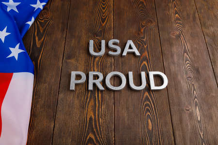 words USA proud laid with silver metal letters on brown wooden surface with flag of United States of...