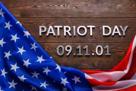 the words patriot day laid with silver metal letters on wooden board surface with crumpled usa flag