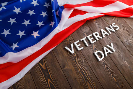 the words veterans day laid with silver metal letters on wooden board surface with crumpled usa flag at right side with diagonal perspectiveの写真素材