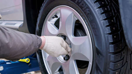 person in winter jacket and white cotton gloves screwing in lug nuts during tire change to studded onesのeditorial素材