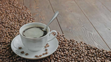 white hand stirring black coffee in a mug on a table covered with roasted coffee beans