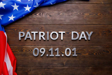 the words patriot day 09.11.01 laid with silver metal letters on wooden board surface with crumpled...