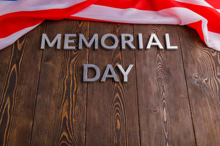 the words memorial day laid with silver metal letters on wooden board surface with crumpled usa flag below.の写真素材