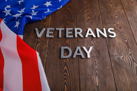 the words veterans day laid with silver metal letters on wooden board surface with crumpled usa flag.の写真素材