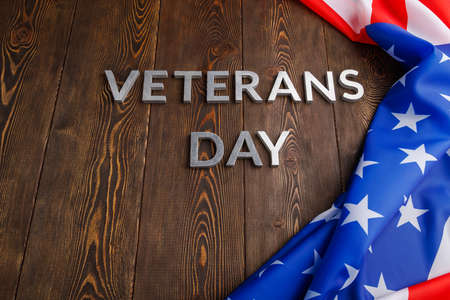 the words veterans day laid with silver metal letters on wooden board surface with crumpled usa flag.の写真素材