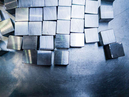 pile of small machined shiny steel cubes on metal surface, closeup with selective focusの写真素材
