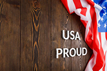 words USA proud laid with silver metal letters on brown wooden surface with flag of United States of...