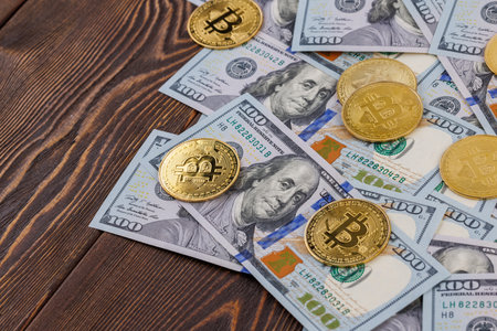 bitcoin coins scattered over US dollar paper banknotes on wooden backgroundの写真素材