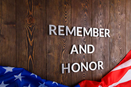 words remember and honor laid with silver metal letters on wooden background with USA flag underneathの写真素材