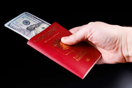 caucasian hand holding russian international passport with inserted US dollars