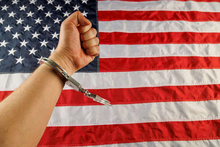 caucasian hand cuffed with silver metal handcuffs over US flag backgroundの写真素材