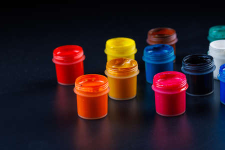 close-up background of opened small gouache paint jars on black surface