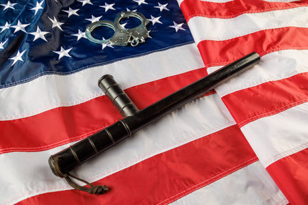 silver metal handcuffs and police nightstick over US flag on flat surface
