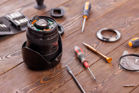 half-disassembled camera zoom lens on wooden table surrounded with toolsの写真素材