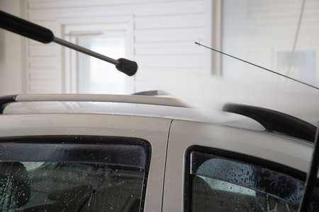 A process of flushing soap sud on silver car roof with pressurised water stream at self-service indoor car wash stationの写真素材