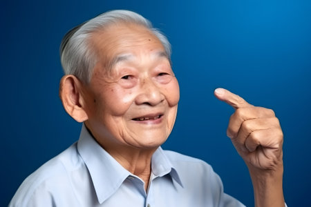 Asian grandfather looking and smiling with rised index finger on blue background, neural network generated artの素材