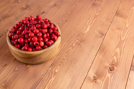 red hawthorn berries in wooden bowl on flat wooden surface.の写真素材