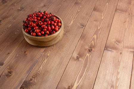 red dog-rose rosehip fruits in a wooden bowl on wooden surfaceの写真素材