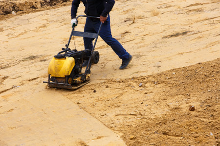 Worker using vibratory plate compactor for compaction sand during path construction at summer day.の写真素材
