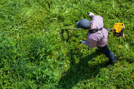 lawnmower man with string trimmer trimming grass at sunny day.の写真素材